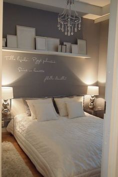 a bed with white sheets and pillows in front of a chandelier hanging from the ceiling