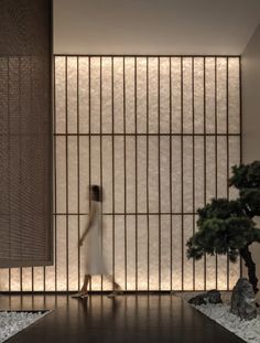 a woman walking in front of a window with bamboo screens on the wall behind her