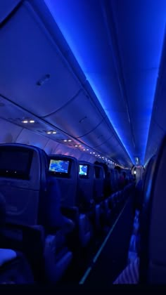 the inside of an airplane with blue lights on it's ceiling and seats down