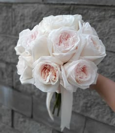 a bouquet of white roses is held by someone's hand against a brick wall