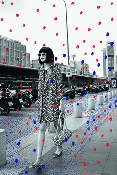 a woman is standing on the sidewalk with red and blue dots all over her