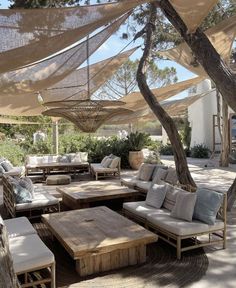 an outdoor seating area with wooden tables and couches, covered by tarps in the shade