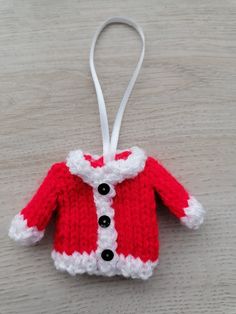 a red and white knitted christmas sweater ornament hanging on a wooden table