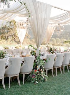 a table set up with white chairs and floral centerpieces for an outdoor wedding