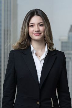 a woman in a black jacket and white shirt standing in front of some tall buildings