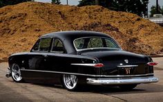 an old black car parked in front of a pile of dirt