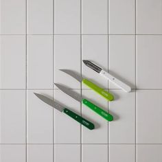 three knives on a white tiled surface with green and red blades next to each other