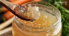 a wooden spoon full of honey sitting on top of a jar filled with liquid next to carrots and broccoli