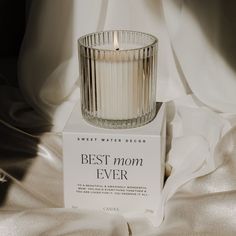 a glass candle sitting on top of a box next to a white sheet covered bed