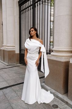 a woman in a white dress standing on the sidewalk