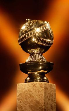 a golden globe on top of a marble block in front of a brown wall with spotlights