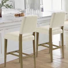 two white bar stools sitting in front of a kitchen counter