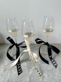 three wine glasses with black ribbon and white wine in them, sitting on a table