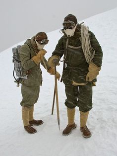 two people standing in the snow with skis and equipment on their hands, one holding a pole