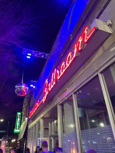 people are standing outside of a building with neon signs on the front and side of it