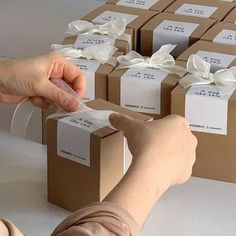 a woman is wrapping packages with white ribbon and bows on the top, while another person reaches for them