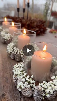 candles are lined up on a table with flowers and pine cones