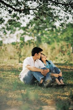 a man and woman are sitting under a tree in an open field, one is holding the other's head