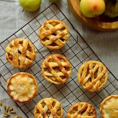 several small pies on a cooling rack next to some apples