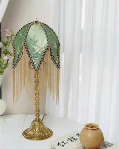 a green lamp sitting on top of a white table next to a vase with flowers