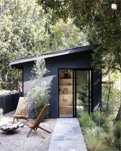 a small black building surrounded by greenery and trees in the back ground is a wooden lawn chair with an open door