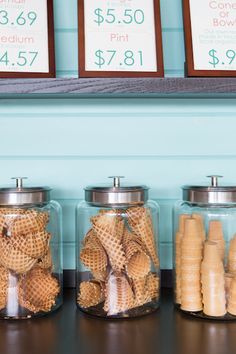 three glass jars filled with different types of sand in front of price signs on the wall