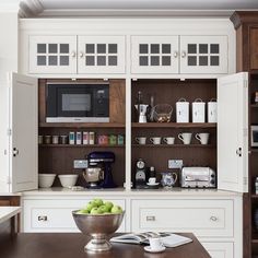 a kitchen with wooden cabinets and white cupboards filled with dishes, coffee maker and green apples