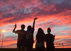 four people standing in front of a sunset with their arms up and one person raising his hand