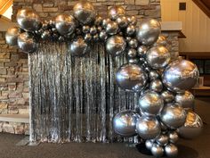 a bunch of silver balloons hanging from the side of a brick wall in front of a fireplace