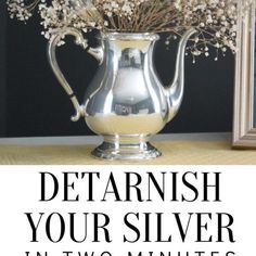 a silver pitcher filled with flowers on top of a table next to a framed photo