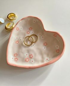 two wedding rings are placed in a heart shaped bowl next to some gold ring holders