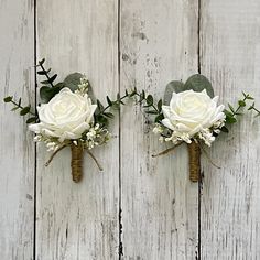 two boutonnieres with white roses and greenery hang on a wooden wall