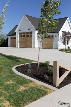 a white house with two garages and a tree in the front yard