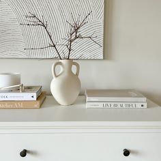 a white vase sitting on top of a dresser next to books