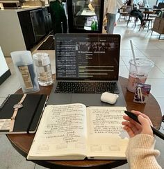 a person sitting at a table with an open book in front of a laptop computer