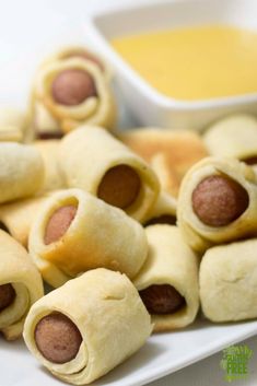 there are many small pigs in a blanket on the plate next to some dipping sauce