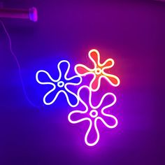 two neon lights that look like flowers on a purple background, one with yellow and pink petals