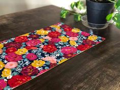 a wooden table topped with a potted plant and a colorful place mat on top of it