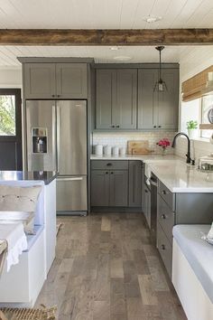 a kitchen with gray cabinets and white counter tops, along with wood flooring that matches the ceiling