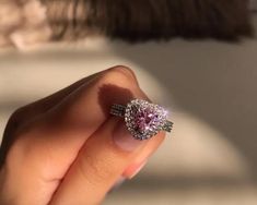 a woman's hand holding a pink diamond ring