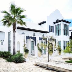 a large white house with palm trees in the front yard and landscaping on both sides