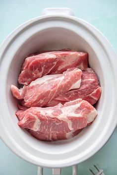 raw meat in a white crock pot on a blue tablecloth with utensils