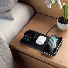 an iphone charging on top of a bed next to a vase with flowers in it