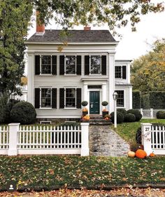 a white house with black shutters and pumpkins