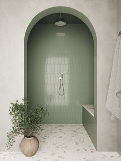 a bathroom with green tile and a plant in the corner, along with white towels