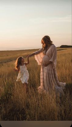 a mother and daughter holding hands while walking through tall grass in the field at sunset