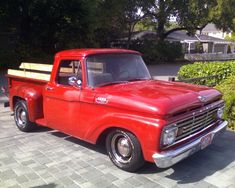 an old red pick up truck parked on the side of the road in front of some bushes