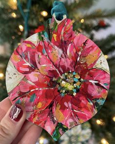 a hand holding a paper flower ornament in front of a christmas tree