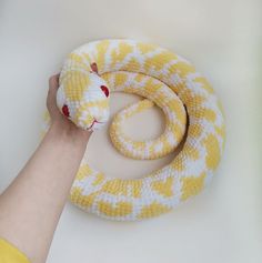 a yellow and white snake is being held by a person's hand on a white surface