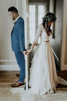 a man and woman standing next to each other in front of an open door wearing wedding dresses